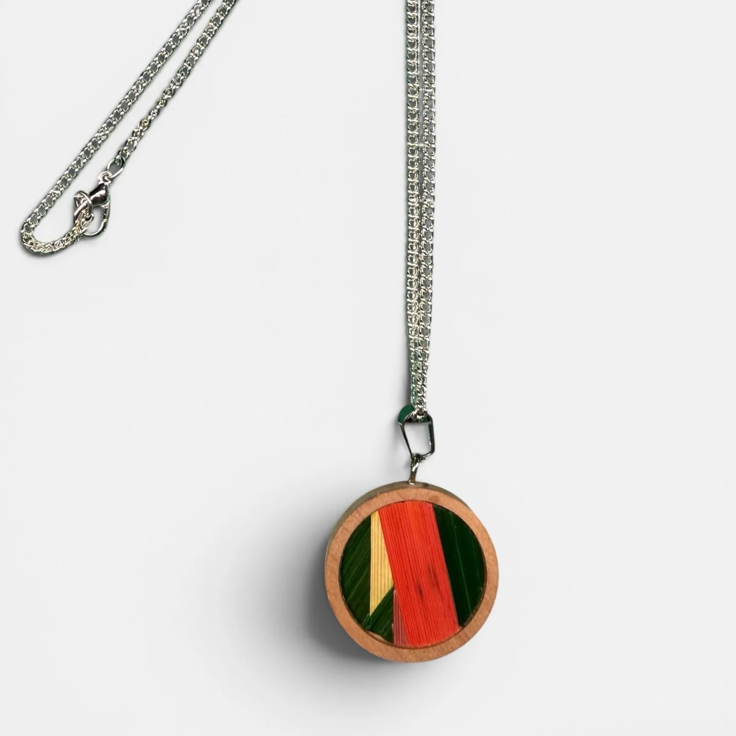 Collier médaillon orange — médaillon rond en bois habillé de marqueterie de paille de seigle teintée vert, jaune et orange, chaîne acier inoxydable argenté, fond blanc